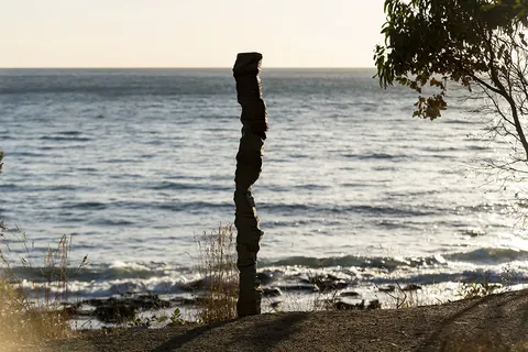 The aluminium column standing on the shoreline with the ocean behind at dusk