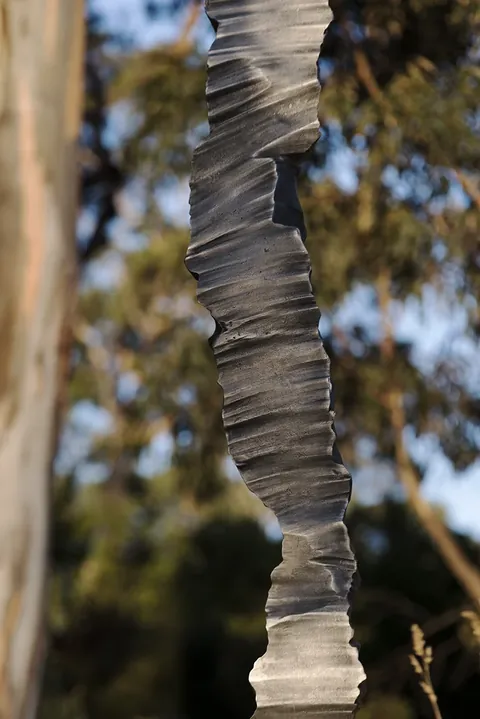 Close view of the column’s layered aluminium surface against gum trees