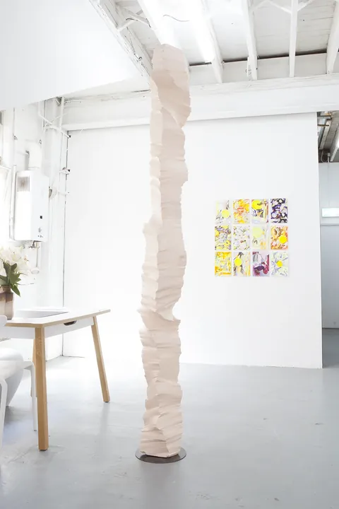 A white polystyrene column in the gallery beside a wall of colourful prints