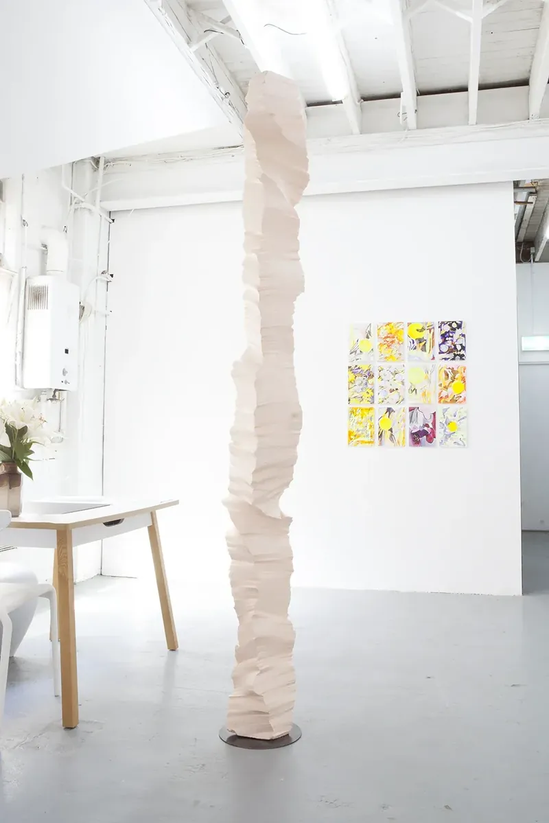 A white polystyrene column in the gallery beside a wall of colourful prints