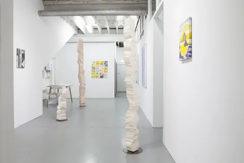 Two white columns in a gallery corridor with paintings on the walls