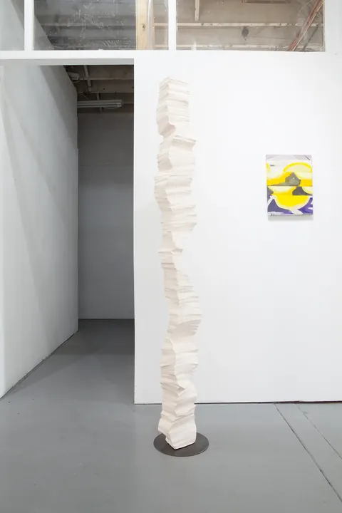 A white column on a dark base by a partition wall with a small painting