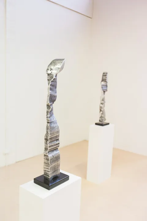 Two polished aluminium columns on white plinths in a gallery
