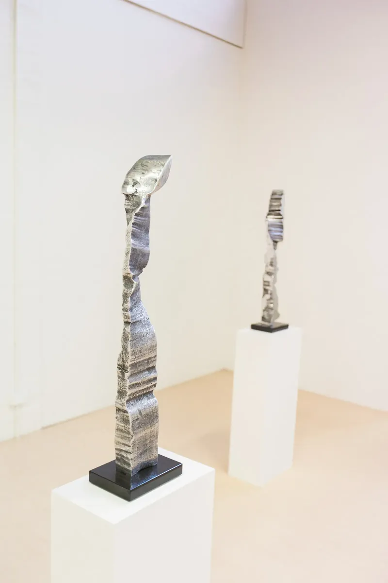 Two polished aluminium columns on white plinths in a gallery