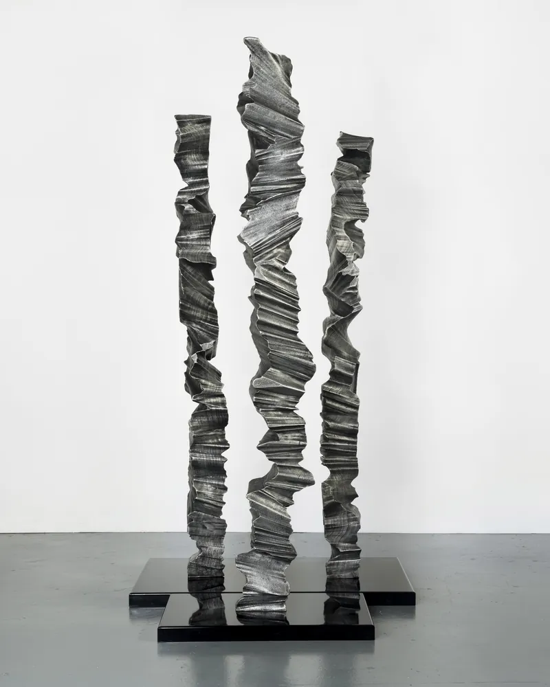 Three aluminium columns of varying heights grouped together on plinths