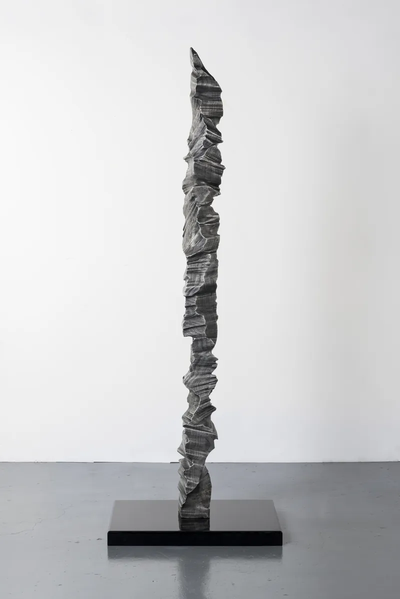 A single aluminium column on a black plinth, full view